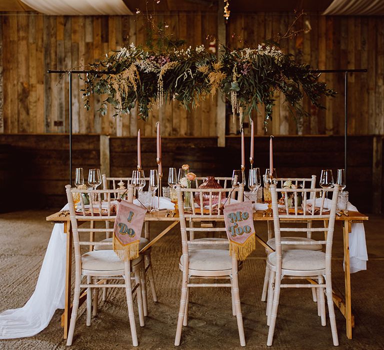 intimate rustic wedding reception table decor with fabric chair back banners and a flower installation 