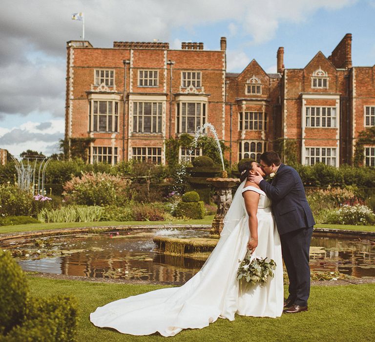 Bride and groom share a kiss in front of pond at Hatfield House 