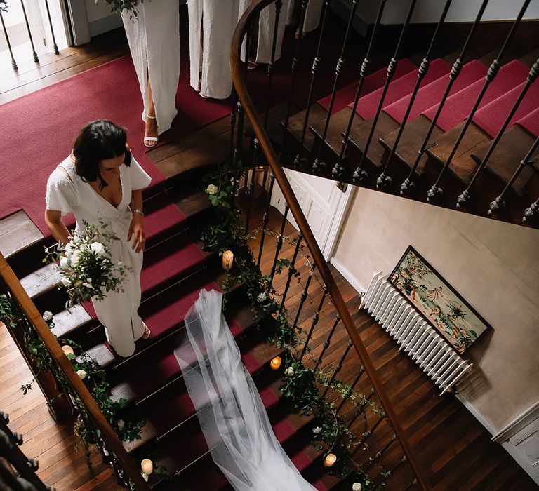 Bridesmaids in sparkly white dresses walk down the stairs behind the bride 