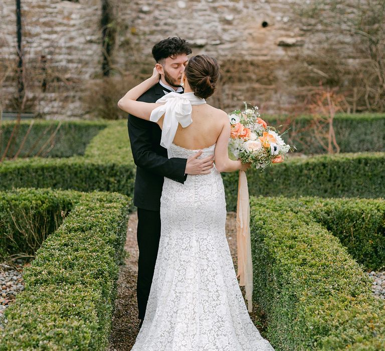 Bride in a lace halter neck wedding dress sitting with her groom in a tuxedo in the gardens at Holesfoot, Cumbria 