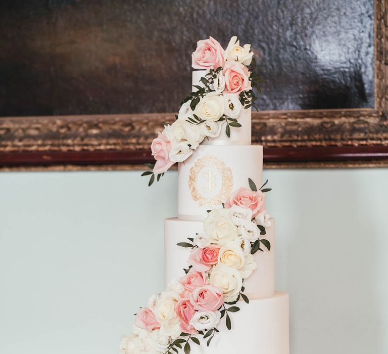 Four tier white wedding cake on white cake stand decorated with pink and white roses with personalised gold detail 