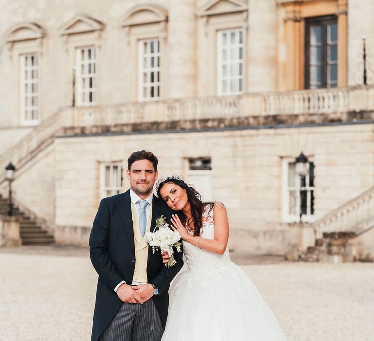 Bride in princess dress rests her head on the groom's shoulder who wears a morning suit with beige waistcoat and blue tie 