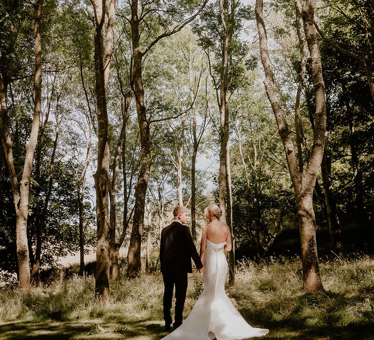 Bride in button back wedding dress stands with groom in black tie as they look at their surroundings 