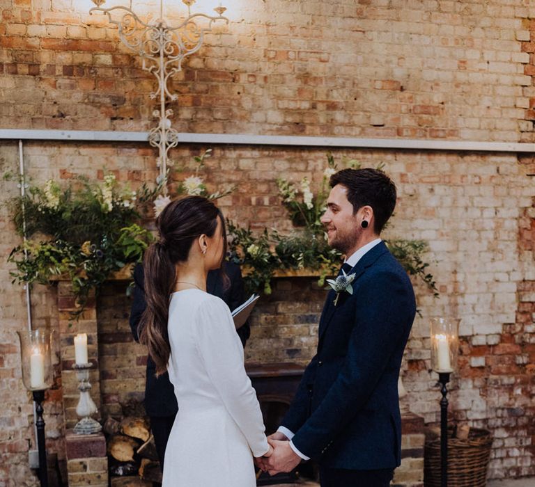 Groom in a blue suit smiles at the bride as they participate in the wedding ceremony 