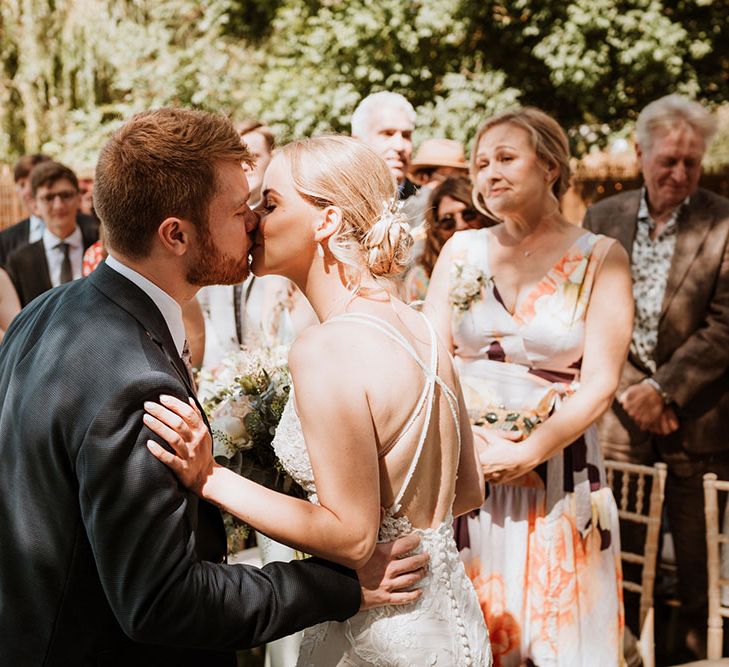 Bride wearing Essense of Australia lace wedding dress with strappy back kisses her groom after wedding ceremony 