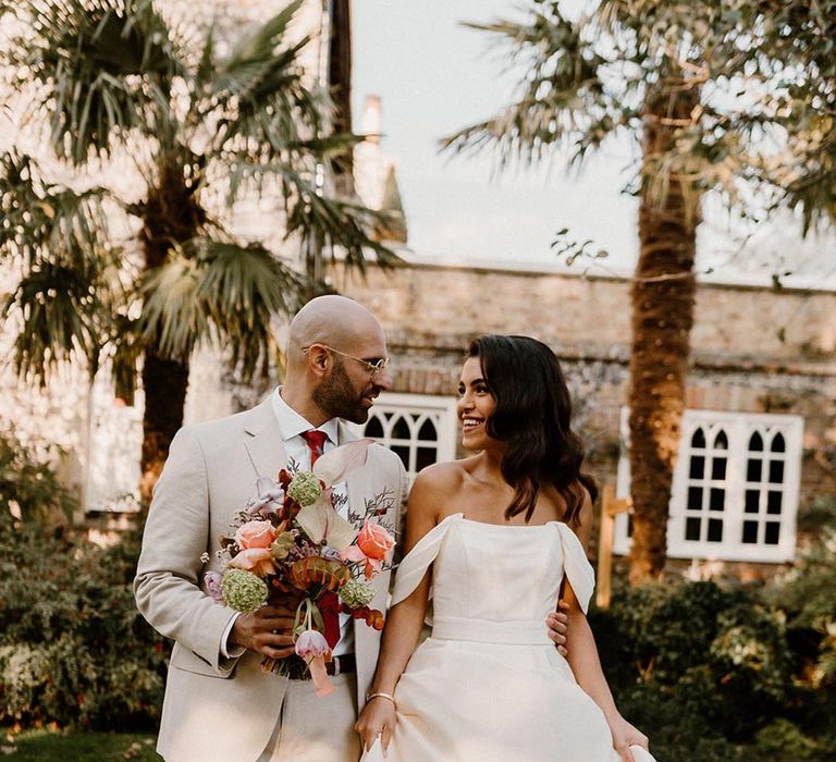 Groom in a pale grey suit with dark red tie and the bride in an off the shoulder wedding dress at the Chapel House Estate