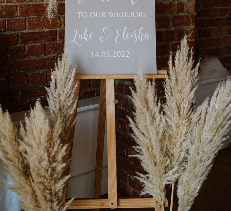 Plexiglass wedding welcome sign with white lettering on wooden easel with dried flower arrangements and burnt orange and toffee roses 