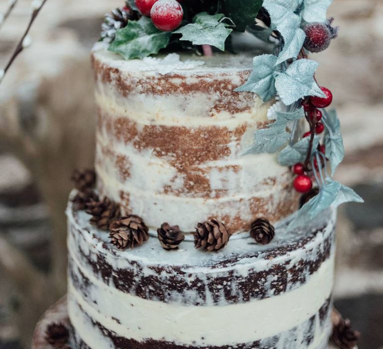 Semi-naked rustic wedding cake with holly, pinecones and berries for decoration