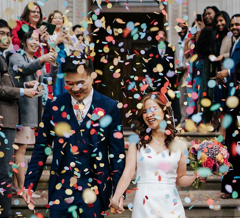 Bride & groom walk through colourful confetti outdoors after wedding ceremony 