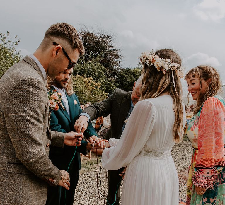 Bride & groom during handfasting ceremony outdoors as bride wears bridal floral crown 