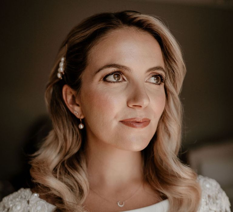 Bride with curled blonde hair with pearl hair clips in a long sleeve fitted wedding dress 