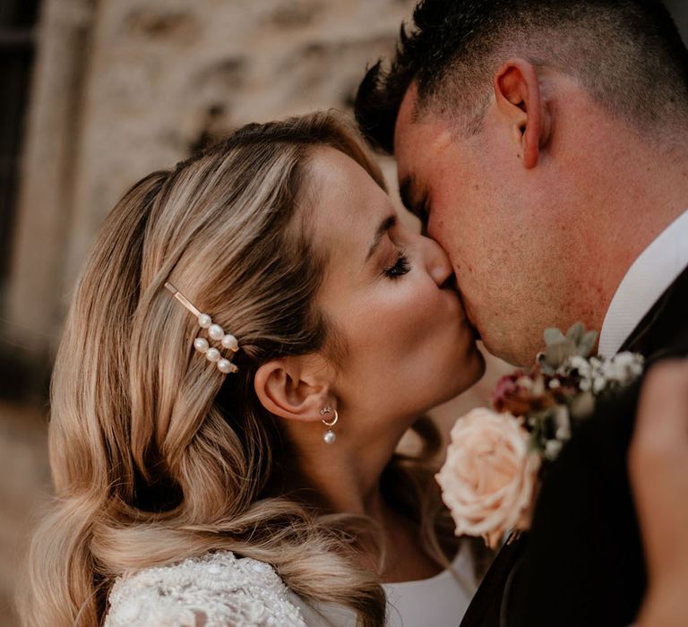  Bride in a beaded long sleeve kissing the groom in black tie with pearl hair clips 