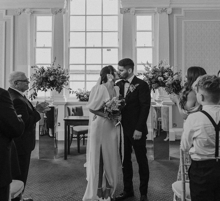 Bride in v neck wedding dress with puff sleeves and front slit and groom in black tux dancing at Somerset House wedding