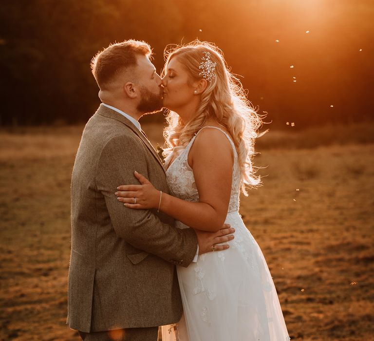 The bride with a sparkly hairpiece kisses the groom during golden hour 