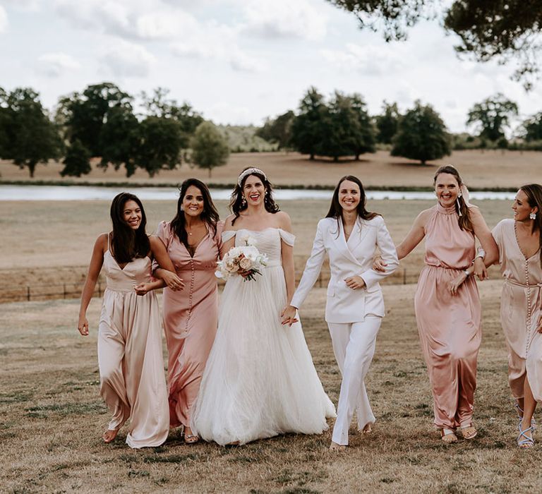 Bridesmaids in pink and champagne dresses with the bride in an off the shoulder wedding dress and bride in white suit 