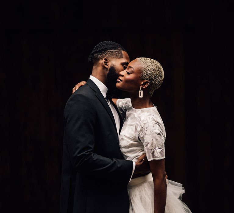 Black Bride and Groom kiss with Bride wearing a bridal two piece set and holding a bridal bouquet full of pink roses, eucalyptus and waxflowers