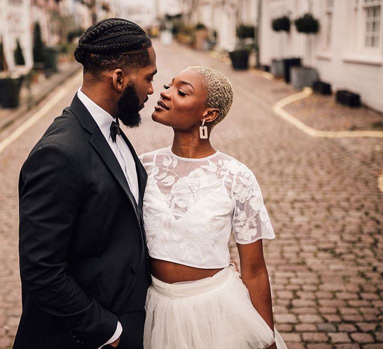 Bride looks at Groom in London mews whilst wearing a floral embroidered top and white ruffled skirt in bridal two piece set