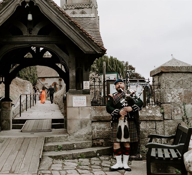 Traditional Scottish bagpipe player stands playing at the entrance to the church 