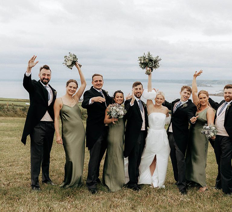 Bride & groom stand with groomsmen in morning suits and bridesmaids in green satin bridesmaid dresses 