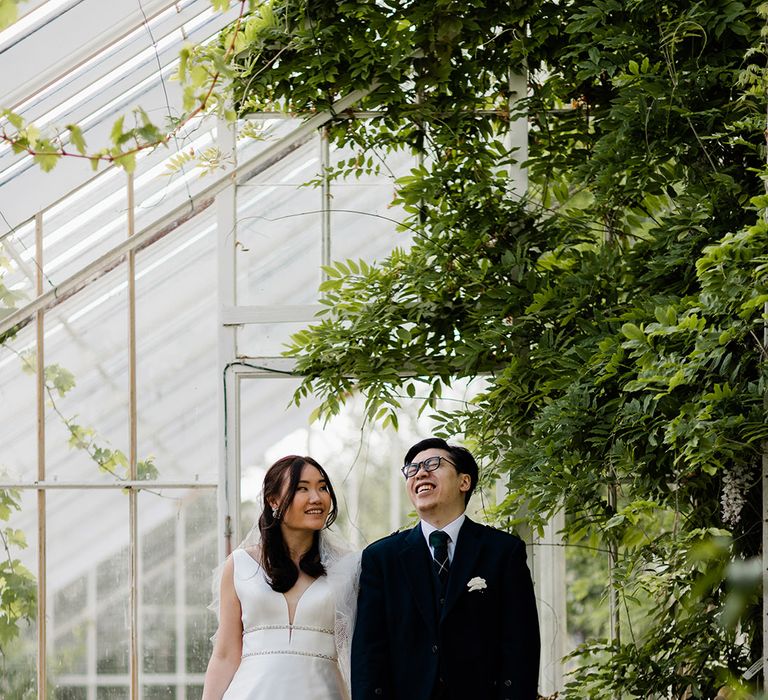 Bride in Princess wedding dress with embellished waistband stands beside her groom in green kilt 