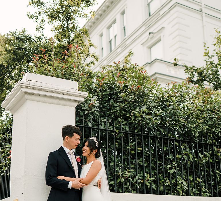 Bride in open back wedding dress with scallop lace edging embraces her groom outdoors during couples portraits