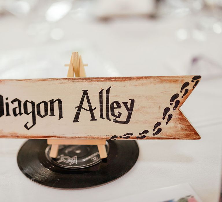 Quirky wedding table number sign in the style of Harry Potter; cream arrow sign with "Diagon Alley" lettering in the Harry Potter font