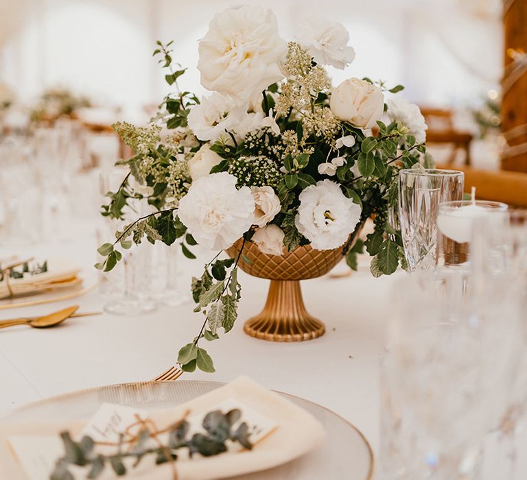 White floral arrangements in gold vases across banquet tables for marquee wedding