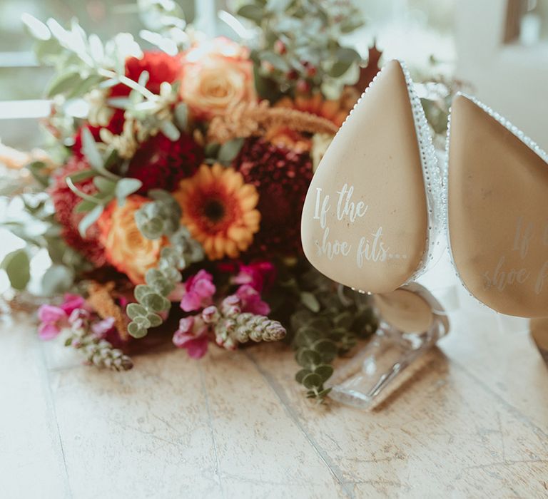 Plastic Cinderella wedding shoes with sparkles and writing on the sole of the shoe with autumnal wedding bouquet 