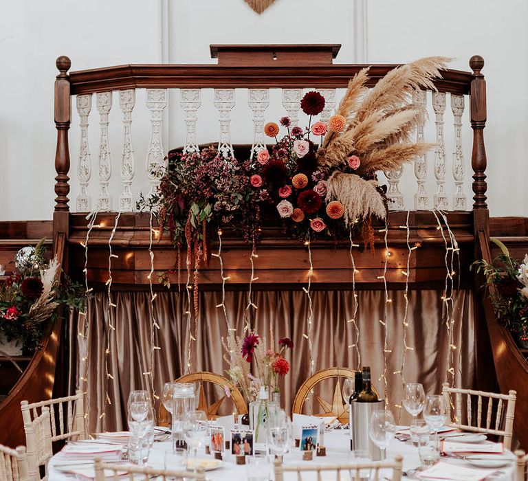 Top table wedding decor with fabric banner, dried and wildflower floral arrangement, gold chairs and string lights 