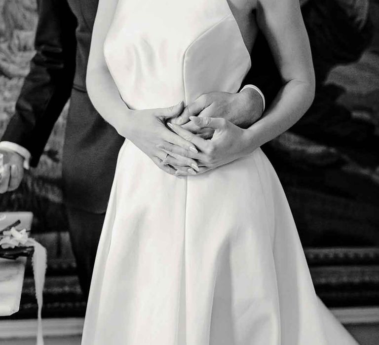 Bride in halterneck wedding dress holding hands with groom in classic black tuxedo 