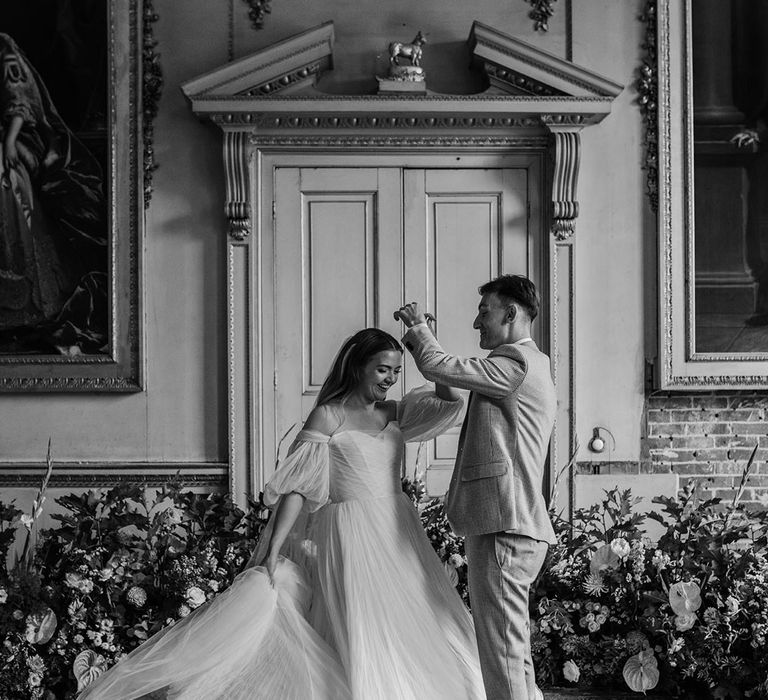 The groom spins the bride around as they stand in front of incredible flower arrangement 