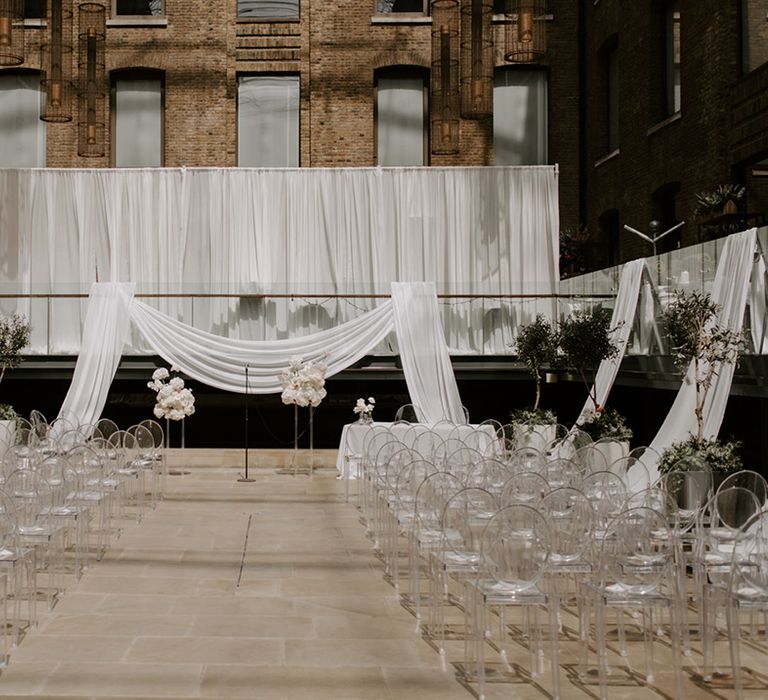 Devonshire Terrace wedding decorated with acrylic chairs and signage, white wedding flowers, and white wedding drapes 