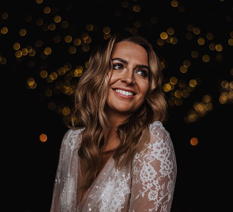 Bride with loosely curled brown hair smiling in her long sleeve sparkly wedding dress 