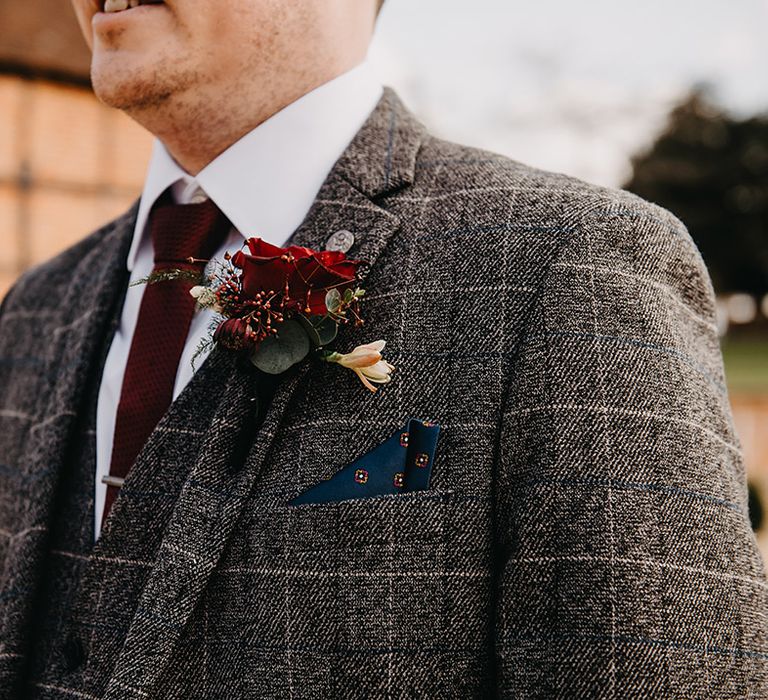 Groom in grey checkered Marc Darcy wedding suit with dark red tie and red rose buttonhole 