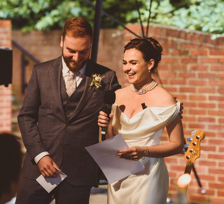 Groom in checkered three piece suit with paisley tie with bride in off the shoulder wedding dress with pearl choker necklace 