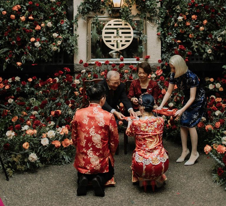 The bride and groom kneel before the groom's parents to serve them tea 