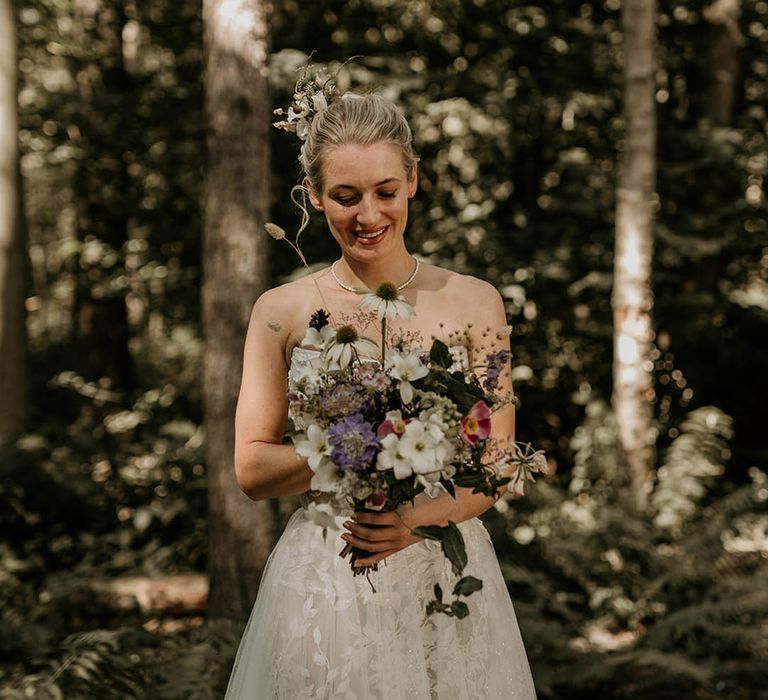 Bride in strapless Milla Nova wedding dress with purple and white wedding bouquet made up of wildflowers 