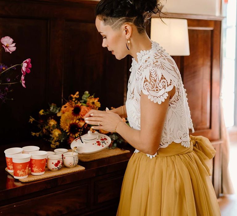 Bride in white mesh lace bridal crop top and yellow wedding skirt partaking in Chinese Tea Ceremony at Broadfield Court