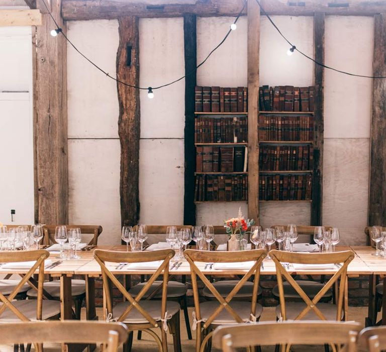 Templars Barn wedding reception room with classic rustic wedding tablescape with floral centrepieces on wooden tree stumps, bookshelves with vintage books and hanging fairylights