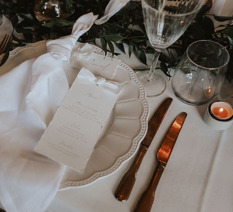 All white wedding place setting with white plates and white wedding menus 