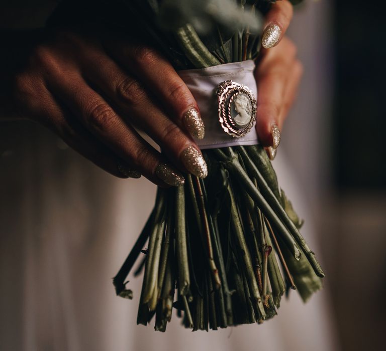 Bride wearing sparkly silver glitter wedding nails holding bouquet tied with a ribbon and brooch 