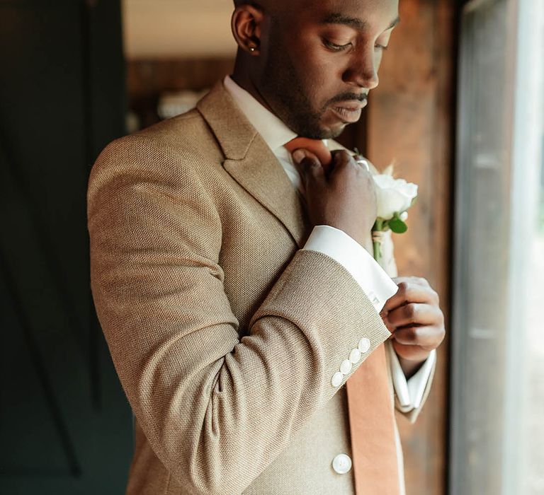 Groom in beige wedding suit with orange tie and white flower buttonhole 