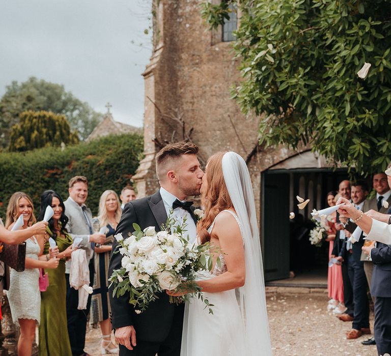 The bride and groom kiss as wedding guests throw confetti over the couple 