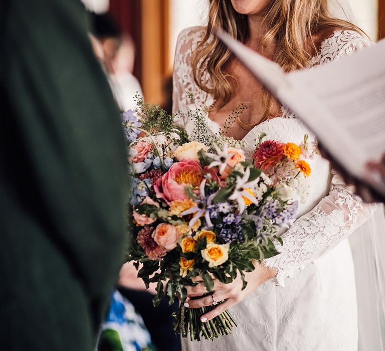 Bride in long sleeve lace wedding dress holding a colourful wedding bouquet at The Cherry Barn in Rye