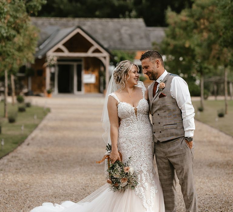 Bride in lace mermaid wedding dress with the groom in a waistcoat at rustic wedding venue 