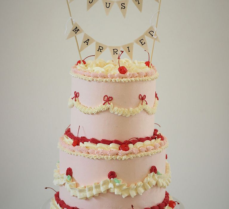 Two tier light pink, white and red iced retro wedding cake decorated with cherries and personalised bunting cake topper 