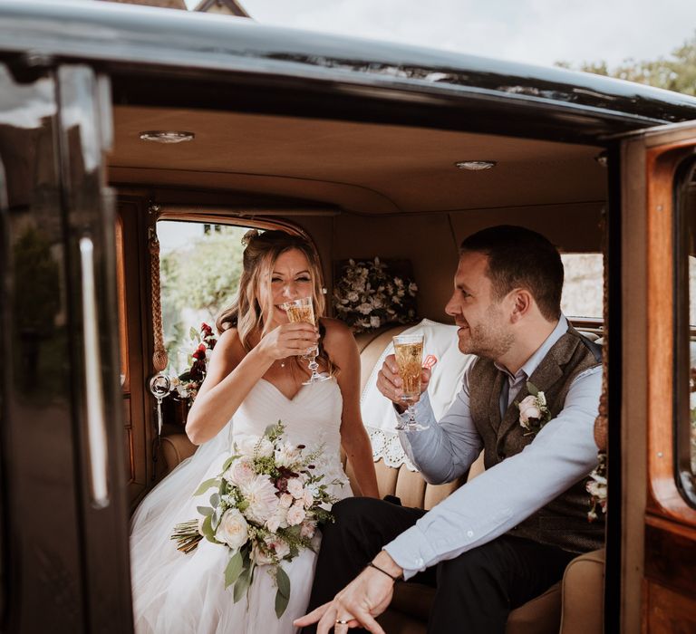 Bride and groom sipping champagne in their vintage wedding car