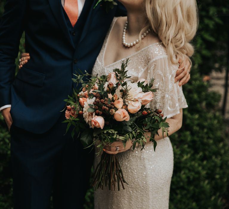 Bride & groom embrace whilst bride holds floral bouquet 