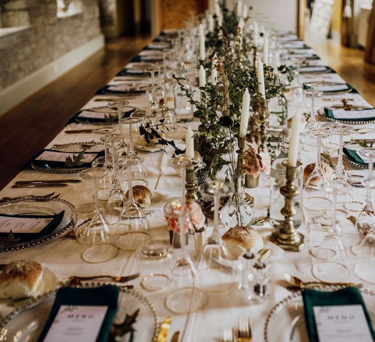 Rustic boho barn wedding table settings with candles, green napkins and gold tableware