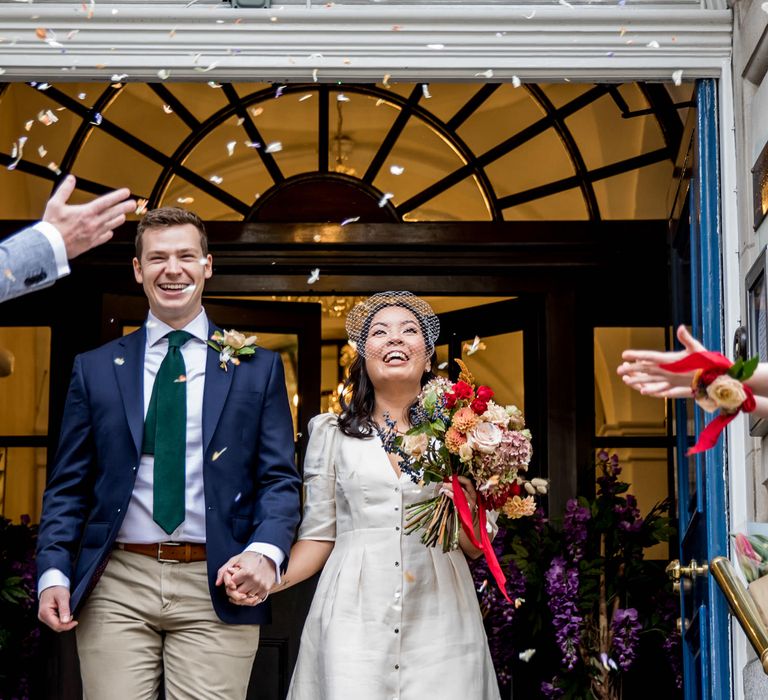 Confetti moment with the bride in a short wedding dress and the groom in chinos and navy blazer exiting